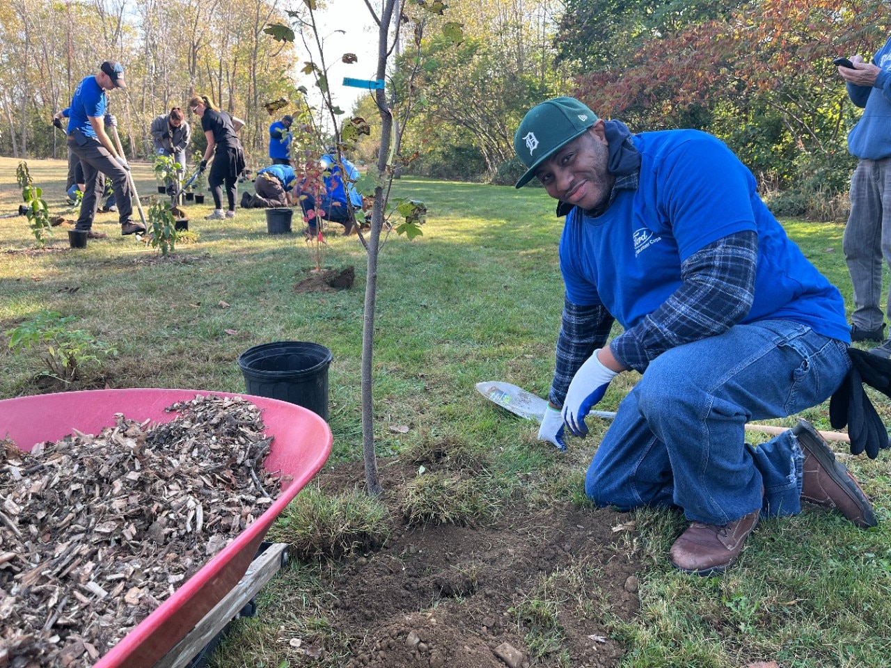 Ford employee smiling next to newly planted tree