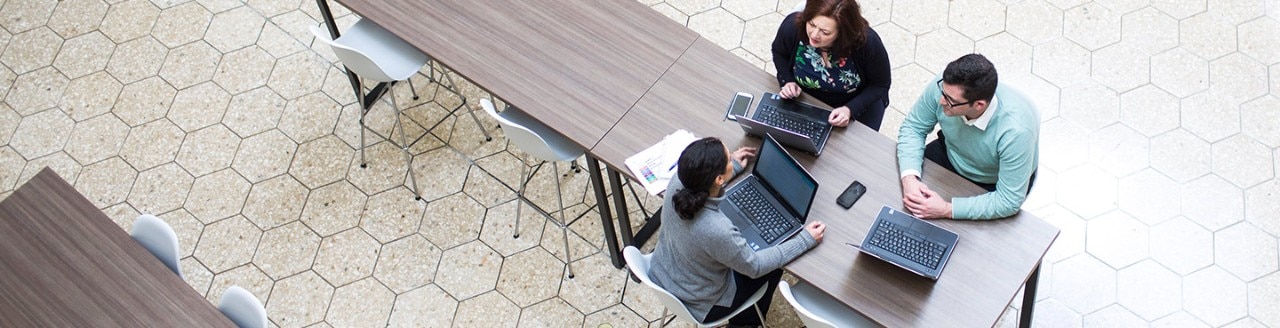 Three people working with laptops in a cafeteria