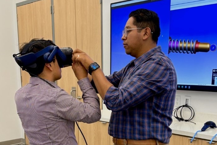 A man wearing a virtual reality headset assists another man, demonstrating the use of VR technology for guidance.