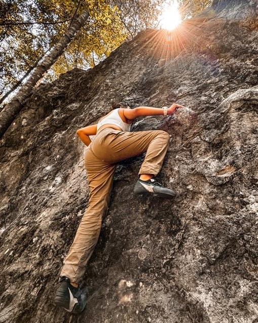 A woman climbs a sunlit rock face, showcasing determination and skill in an outdoor climbing adventure.
