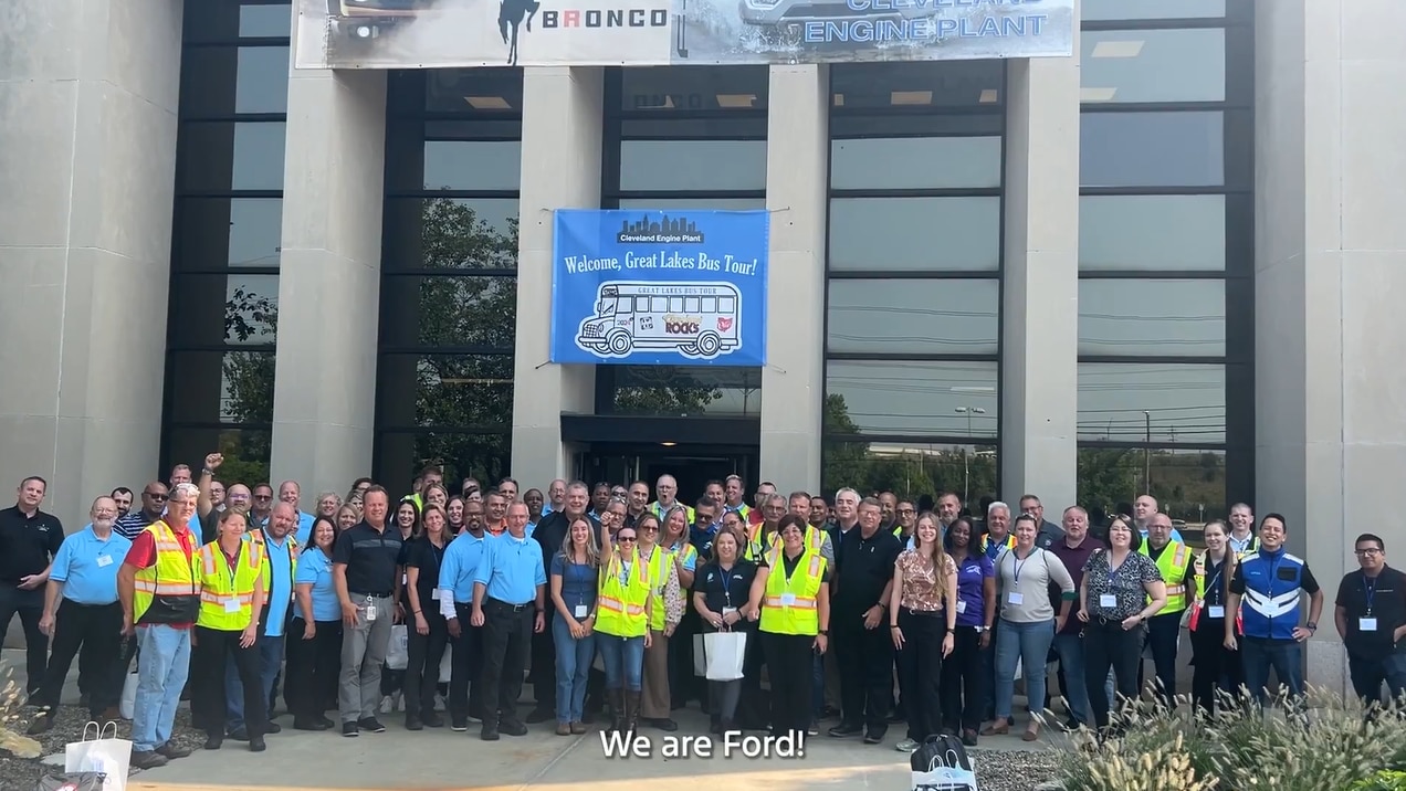 Large group of manufacturing plant employees in front of engine plant smiling