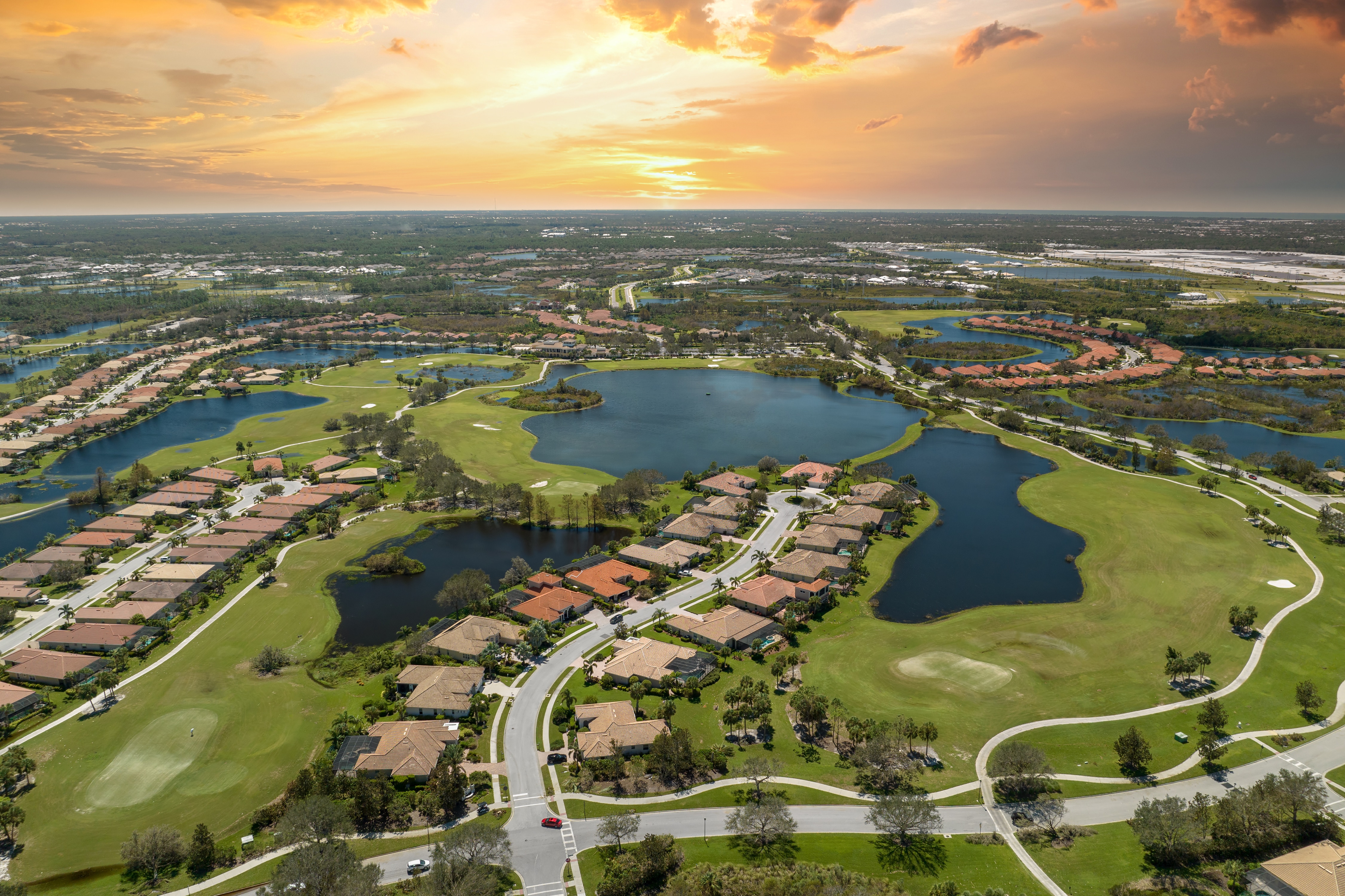 Aerial view of a golf course surrounded by residential homes, bathed in warm hues of sunset.